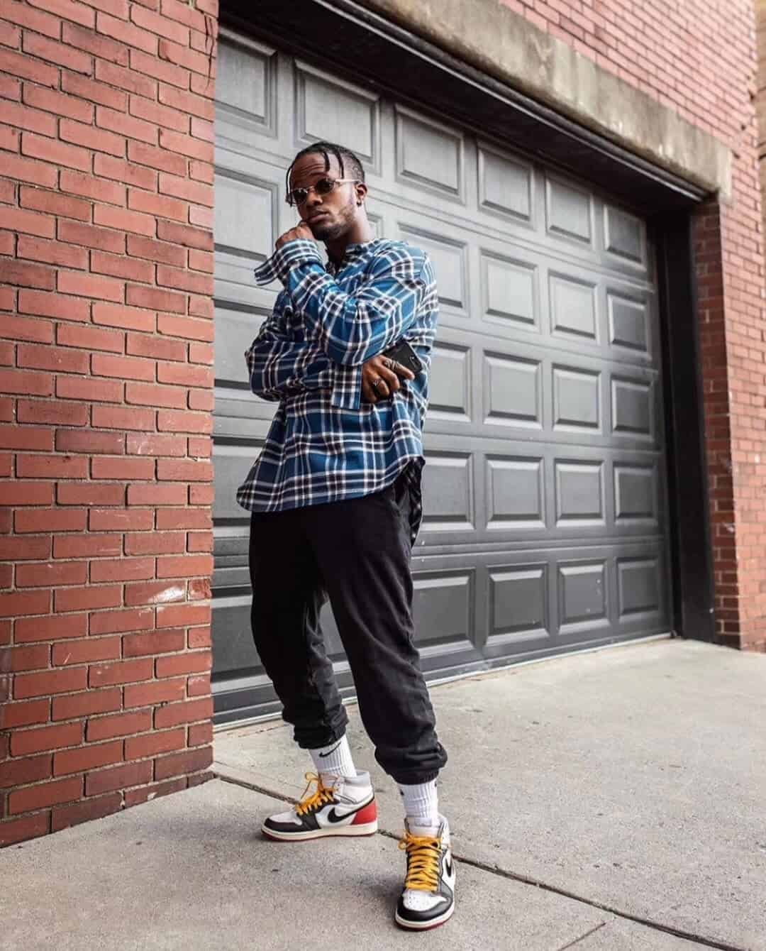 Blue plaid shirt, casual streetwear, man with sunglasses, standing in front of a garage door, urban fashion style, cool vibe, trendy accessories, confident pose.